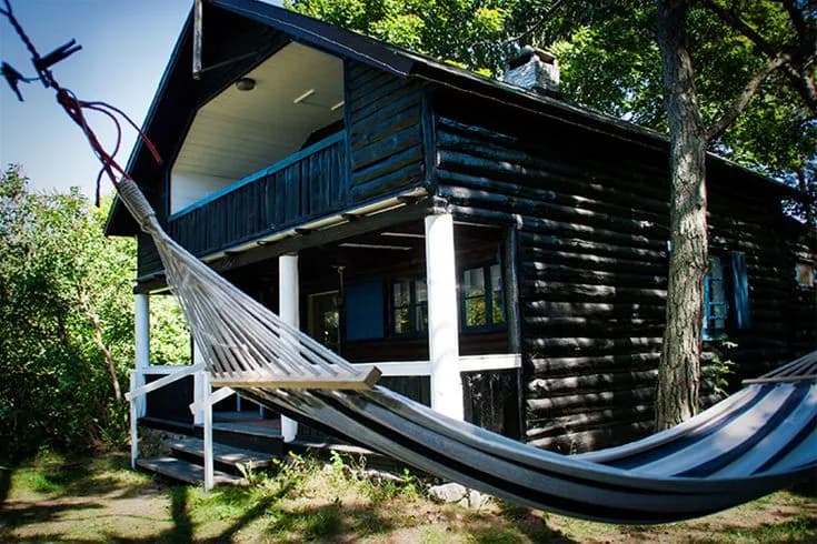 En mysig trästuga med veranda i skuggan, omgiven av en grönskande gårdsplan, vid Tofta Camping.