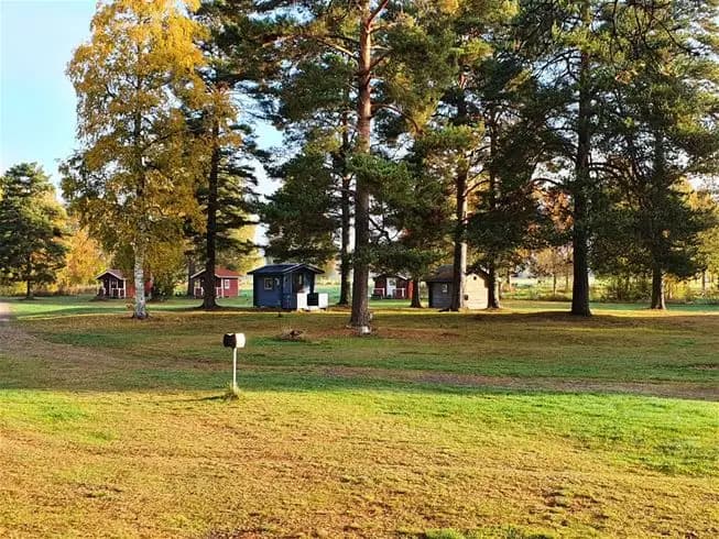 Bild av Nås Camping med grönt gräs och träd i förgrunden. En vidsträckt gräsyta sträcker sig ut mot horisonten där fler träd skapar en naturskön och fridfull atmosfär.