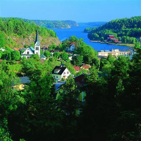 En naturskön vy över Grännäs Camping och Stugby med grönskande vegetation intill en vattenväg, omgiven av ett landskap med rik flora.