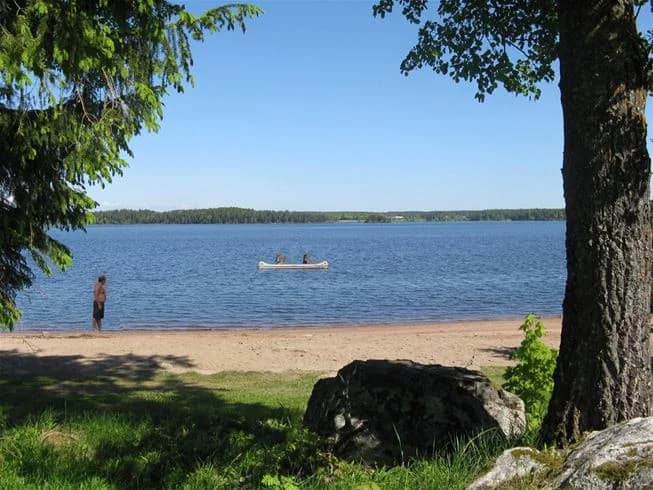 En somrig vy över vattnet vid Falkudden camping, med blå himmel, öppet vatten och grönskande strandlinje.