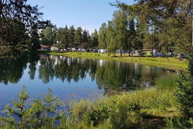 En fridfull campingplats vid Vivstavarvstjärn med gröna träd och växter som speglas i det stilla vattnet.