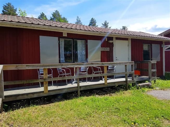 En rustik timmerstuga med en veranda, omgiven av en välskött trädgård på Vivstavarvstjärns camping.