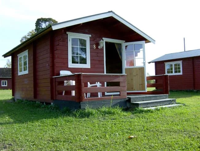 En trästuga med en svart dörr och rött tak omgiven av gröna gräsmattor, belägen vid Storängens camping, stugor & outdoor.