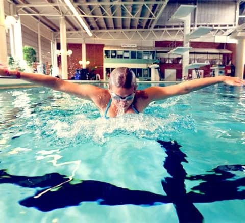 En stor pool med glada människor i badkläder som njuter av sin semester på Gustavsvik Resort. Vissa bär simglasögon och deltar i olika fritidsaktiviteter.