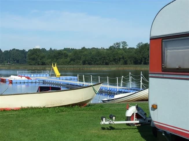 En stilla sjö vid Jägersbo Camping Swecamp med flera små båtar förtöjda vid stranden, omgiven av lummig grönska och ett landskap av vattendrag och våtmarker.
