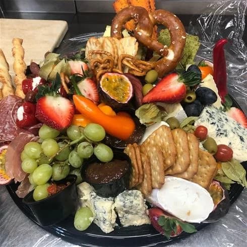 En närbild av ett inbjudande matbord utomhus på Degernäs Camping. På bordet syns en riklig mängd färska frukter, aptitretande småplock samt olika delikatesser. Tallrikar och bestick är prydligt placerade, redo för en måltid i naturen.