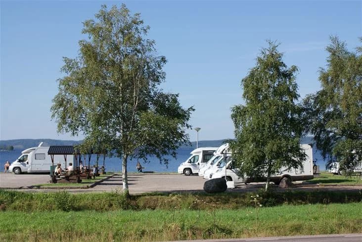 Bilden visar en parkeringsplats vid Sandaholm Restaurang & Camping med flera olika fordon, inklusive lyxbilar, sportiga terrängfordon och husbilar.