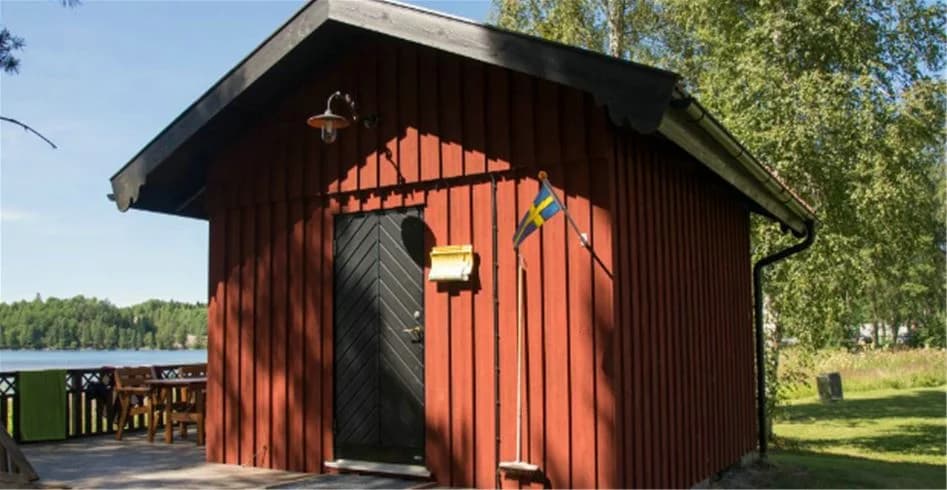 En bild av Sandaholm restaurang & camping visar en mysig träbyggnad omgiven av grönska. Byggnaden liknar en stuga eller timmerstuga och är placerad i en naturskön miljö, vilket skapar en inbjudande atmosfär för besökare.