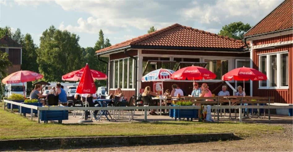 En utomhusmiljö med picknickbord och stolar på Sandaholm restaurang & camping, där besökare kan njuta av avkoppling och fritidsaktiviteter under semestern.