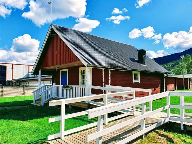 En trästuga med veranda omgiven av en grön gräsmatta vid Sysslebäcks stugby & fiskecamping.