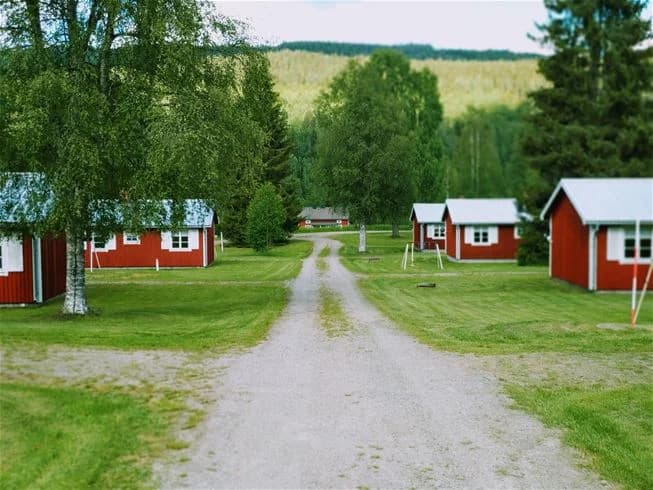 En stuga omgiven av grön gräsmatta och träd i en lantlig miljö vid Sysslebäcks stugby & fiskecamping.