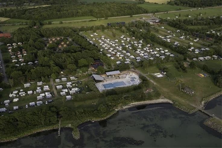 Fågelperspektiv över Lundegård Camping & Stugby med stugor utspridda i ett naturskönt landskap, omgivna av parkgrönska och lantlig charm.
