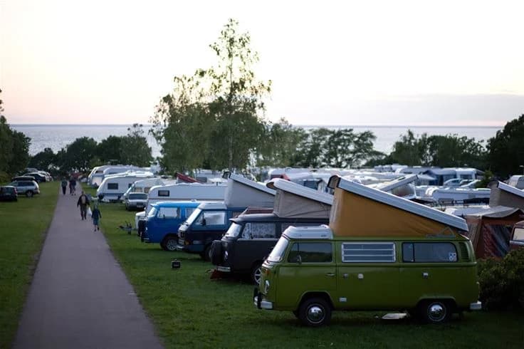 En klassisk Volkswagen husbil parkerad på Lundegård Camping & Stugby, omgiven av andra campingfordon och grönska.