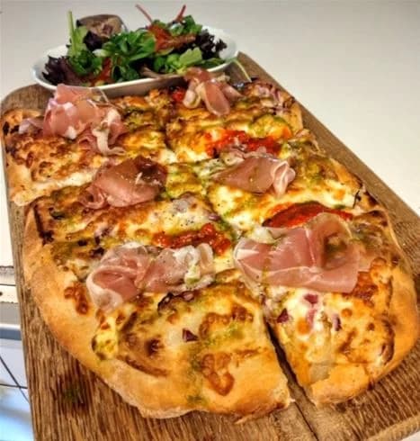 En närbild av en pizza toppad med olika ingredienser som ost och kött, placerad på ett bord.