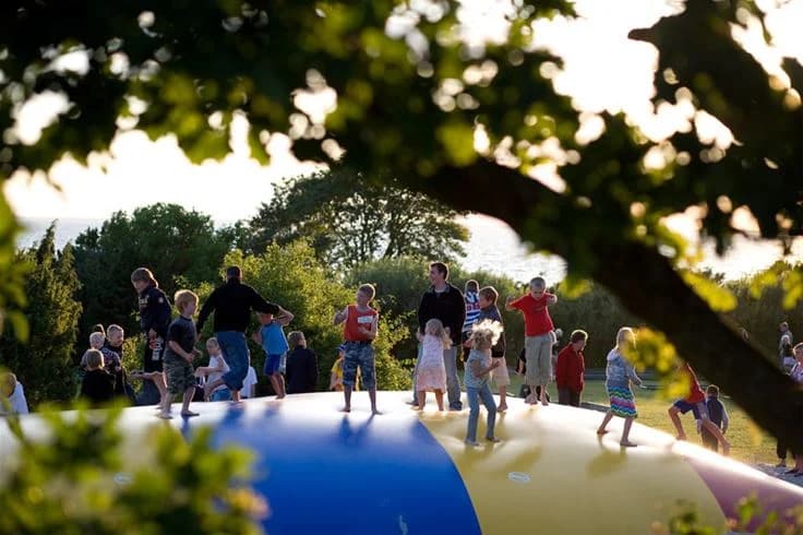 En sommardag på Lundegård Camping & Stugby, med barn som leker på uppblåsbara lekredskap. Människor njuter av utomhusaktiviteter i en grönskande naturmiljö.
