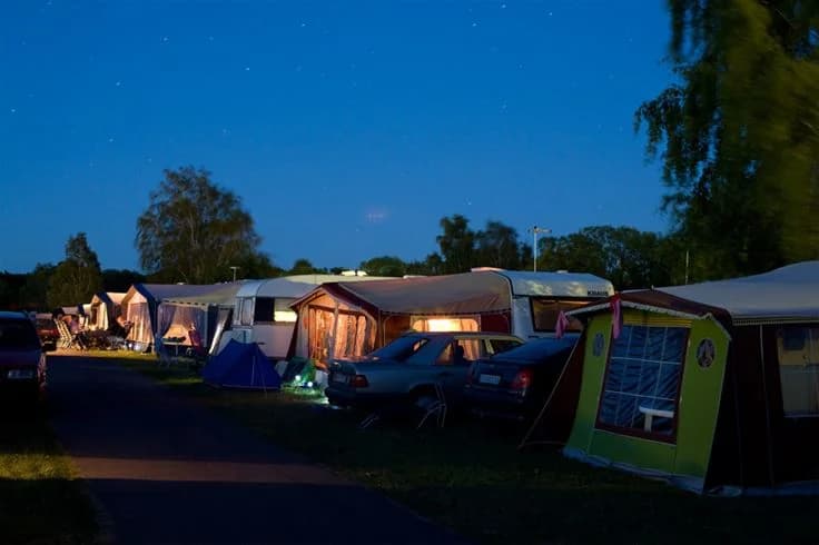 En campingplats på natten med tält och en lastbil parkerad i en lummig parkmiljö på Lundegård Camping & Stugby.