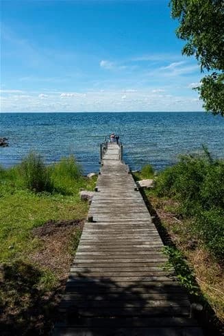 En somrig vy vid Lundegård Camping & Stugby med en träbrygga som sträcker sig ut mot det blåa havet, där horisonten möter en klar sommarhimmel.