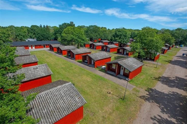 En vidsträckt grön gräsmatta omgiven av träd på Lundegård Camping & Stugby, vilket ger en lugn och naturnära atmosfär i parkliknande miljö.