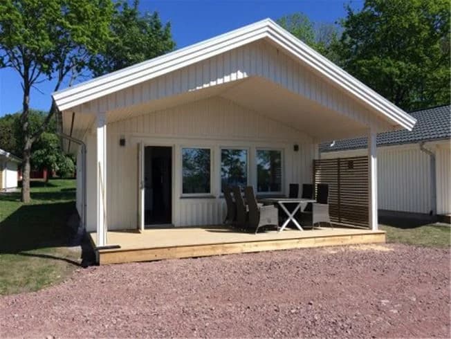 En skuggig trästruktur på Lundegård Camping & Stugby omgiven av lövträd och en välskött gräsyta.