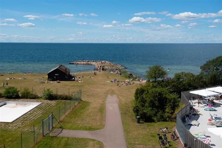 En naturskön kustvy vid Lundegård Camping & Stugby med sandstrand och lugnt blått hav under en klar horisont, perfekt för en avkopplande semester.