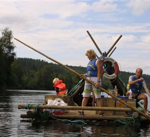 En stilla flod med flera båtar förtöjda längs stranden, omgiven av grönskande natur vid Klarälvens camping.