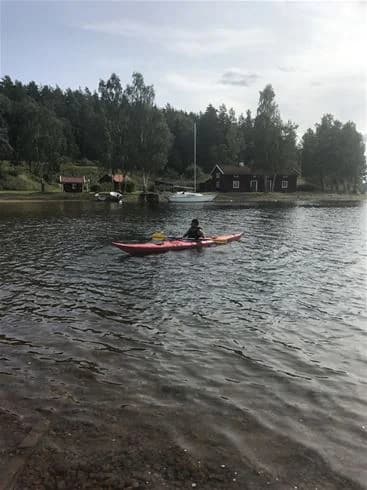 En färgglad kajak flyter på en lugn sjö vid Malexander Camping, omgiven av grönskande natur och en klar blå himmel.