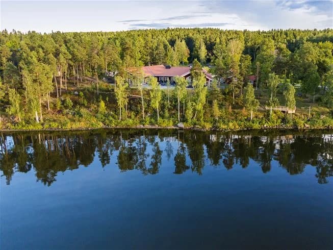 Utsikt över Hjälmargården & Läppe Camping med en vacker vy över en sjö omgiven av frodig skog och naturlandskap, där vattnet sträcker sig längs med stranden och skapar en lugn och avkopplande atmosfär.