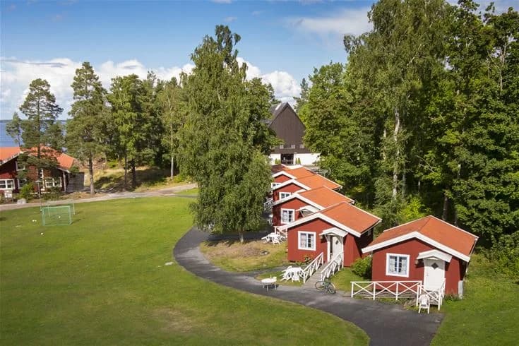 En pittoresk stuga vid ett grönt gräsfält på Hjälmargården & Läppe Camping, med omgivande lugn landsbygd.