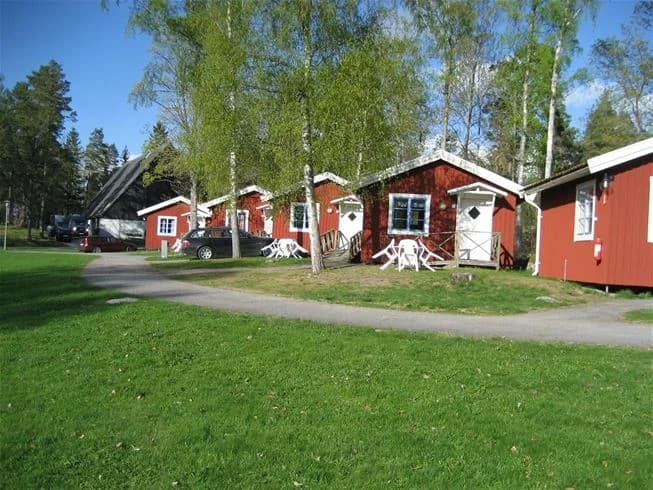 En grönskande campingplats med gräs, träd och en liten stuga, belägen i ett lantligt område vid Hjälmargården & Läppe camping.