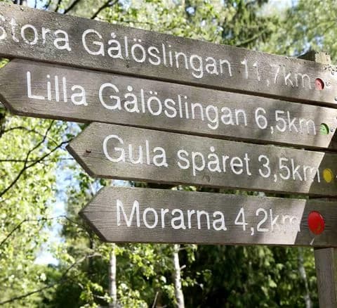 En träskylt vid ingången till ett naturreservat på Gålö havsbad, omgiven av tät skog och naturlandskap.
