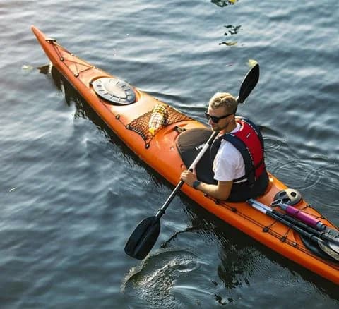 En person paddlar en kajak på det lugna vattnet vid Gålö havsbad, omgiven av skärgårdslandskap.
