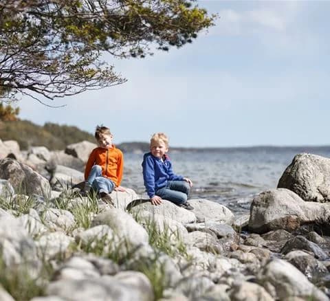 En grupp människor njuter av solen vid Gålö havsbad, omgivna av klippor och kustlandskap. Perfekt för avkoppling och friluftsliv.
