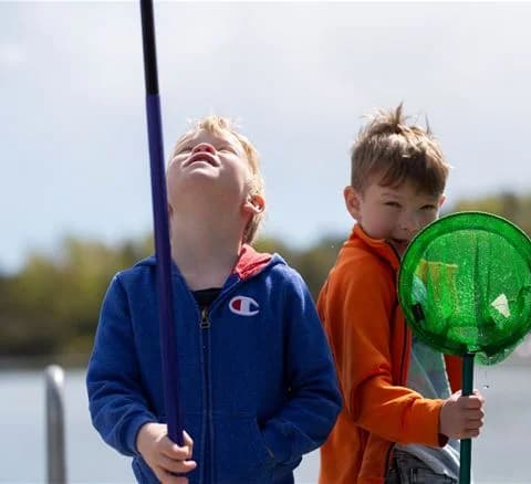 En glad småbarn leker vid Gålö havsbad, omgiven av leksaker och njuter av en solig dag vid stranden.