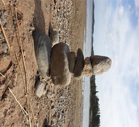 Bild av en naturlig strand vid Gålö Havsbad med stenar och klippblock i olika storlekar utspridda längs den grå sanden.