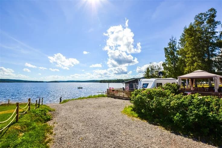 En naturskön camping med husvagnar vid en sjö med skogsklädda stränder, som ger en avkopplande och fridfull atmosfär.