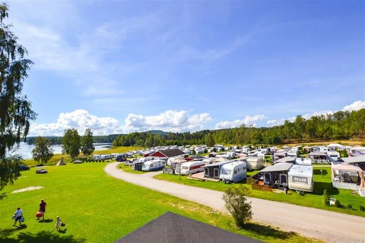 Panoramautsikt över en lugn sjö omgiven av skogsklädda kullar under en himmel med cumulusmoln vid Charlottenberg camping & stugor - Haganäset.