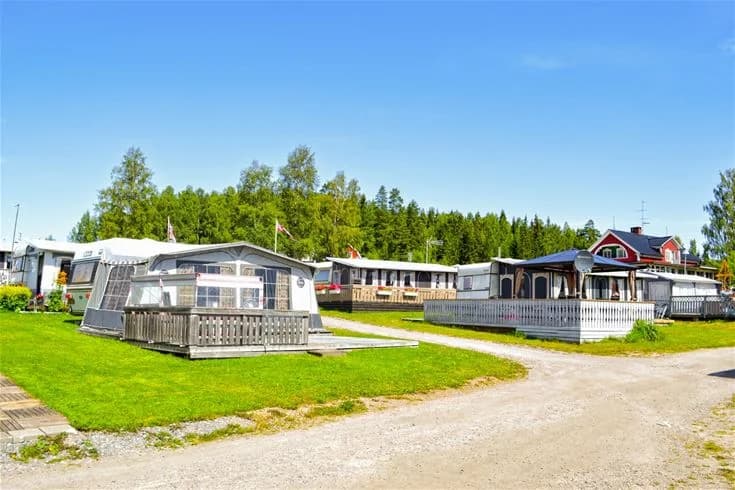 En campingplats med mobila hem och stugor, omgiven av skuggande träd och parkeringsmöjligheter, vid Charlottenberg camping & stugor - Haganäset.