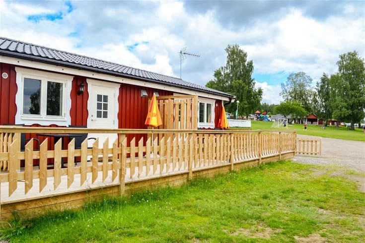 En grönskande campingplats med öppet gräsområde och träd i bakgrunden, vilket skapar en naturnära och rofylld miljö.