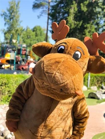 En leende älgmaskot pryder gräsmattan vid Charlottenberg camping & stugor - Haganäset, sprider glädje och semesterkänsla.