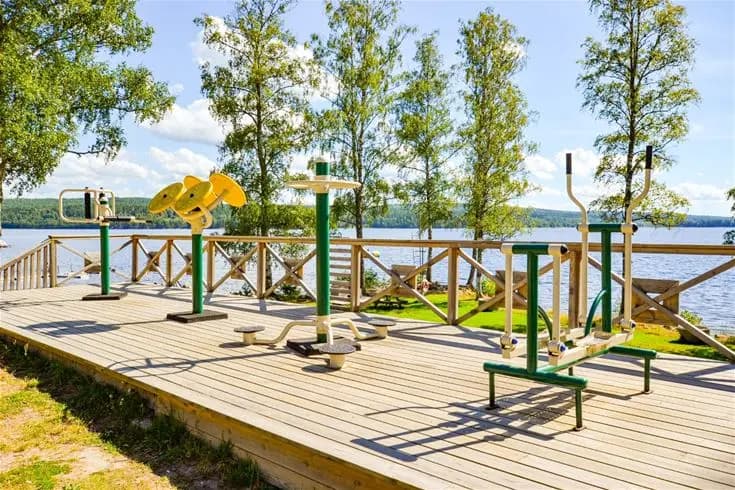 En träbrygga sträcker sig ut över en lugn sjö omgiven av grönskande skog vid Charlottenberg camping & stugor - Haganäset.