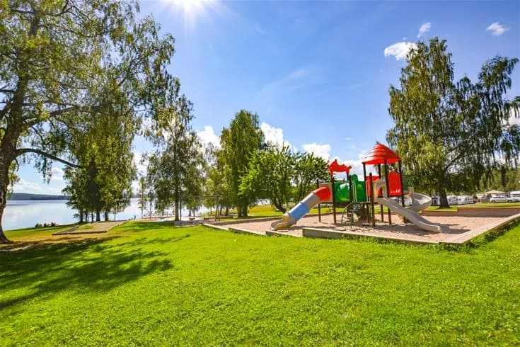 En grönskande campingplats med välskötta gräsmattor och skuggiga träd. Det finns picknickbänkar och utomhusmöbler för besökare att vila och njuta av omgivningen.