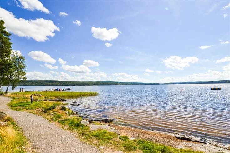 En bild av en sjö vid Charlottenberg camping & stugor - Haganäset, med blå himmel och moln vid horisonten.