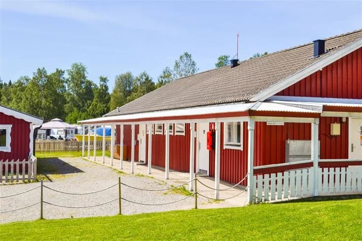 En grönskande campingplats med skuggiga områden och stång, inom Charlottenberg camping & stugor - Haganäset, omgiven av frodig natur.