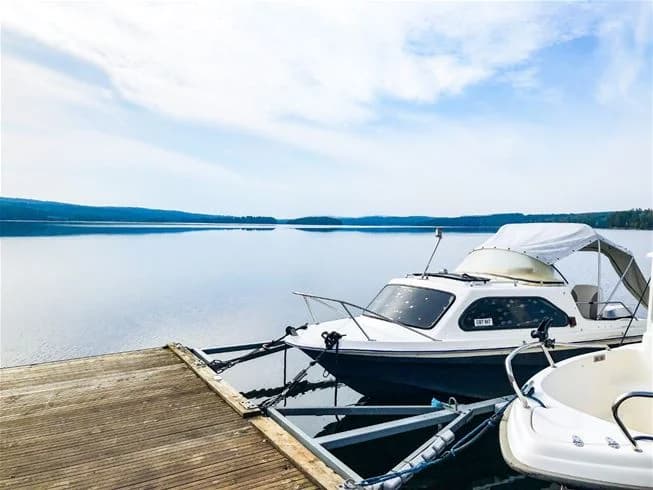 En motorbåt ligger förtöjd vid en brygga på Charlottenberg camping & stugor - Haganäset, med en sjö eller hav i bakgrunden.
