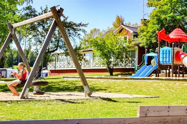 En lekplats med klätterställning och rutschkana, omgiven av grönska, på Charlottenberg camping & stugor - Haganäset. Perfekt för utomhusaktiviteter och lek för barn.