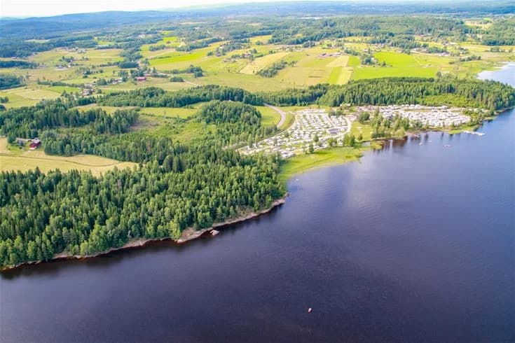 En vacker utsikt över en sjö med klart vatten, omgiven av grönskande landskap, vid campingplatsen Charlottenberg camping & stugor - Haganäset.