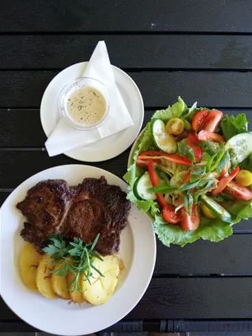 En tallrik med olika maträtter, inklusive stekt kött, grönsaker och andra tillbehör, placerad på ett bord med bestick och serveringsföremål.