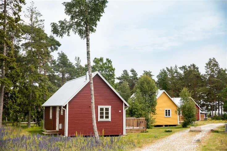 Bild av Ljugarns semesterby & camping med en stuga omgiven av gräs och öppna ytor. Stugans tak syns tydligt och området ger en lantlig och avkopplande känsla.