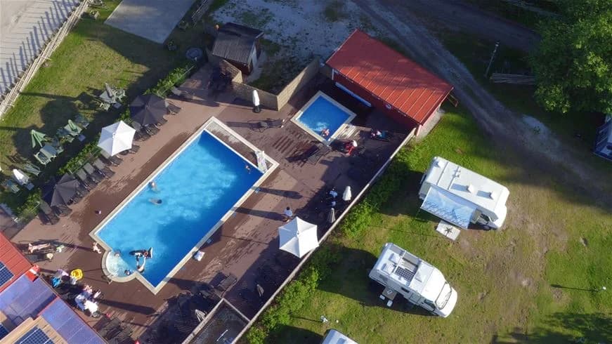 En solig dag vid Ljugarns semesterby & camping med en inbjudande utomhuspool omgiven av solstolar och parasoller, idealiskt för avkoppling och semesterfirande.