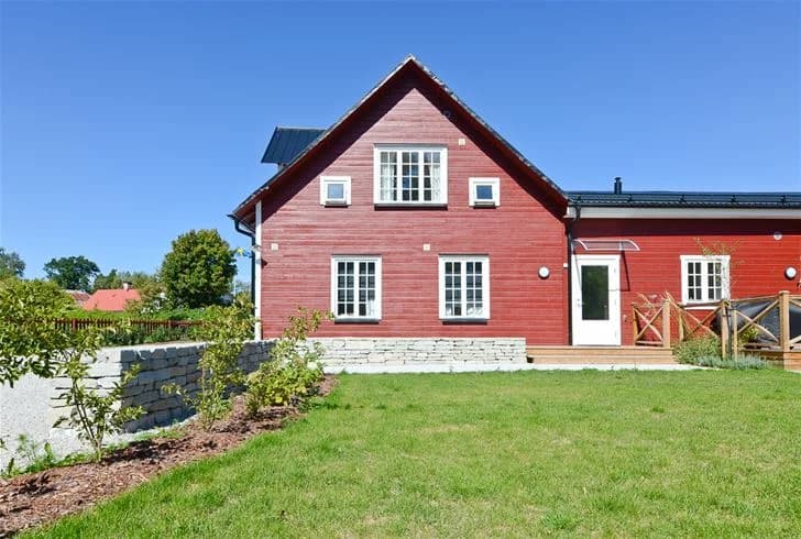 En ljus trästuga med flera fönster och ett snedtak, omgiven av en välskött gräsmatta i ett lugnt bostadsområde.